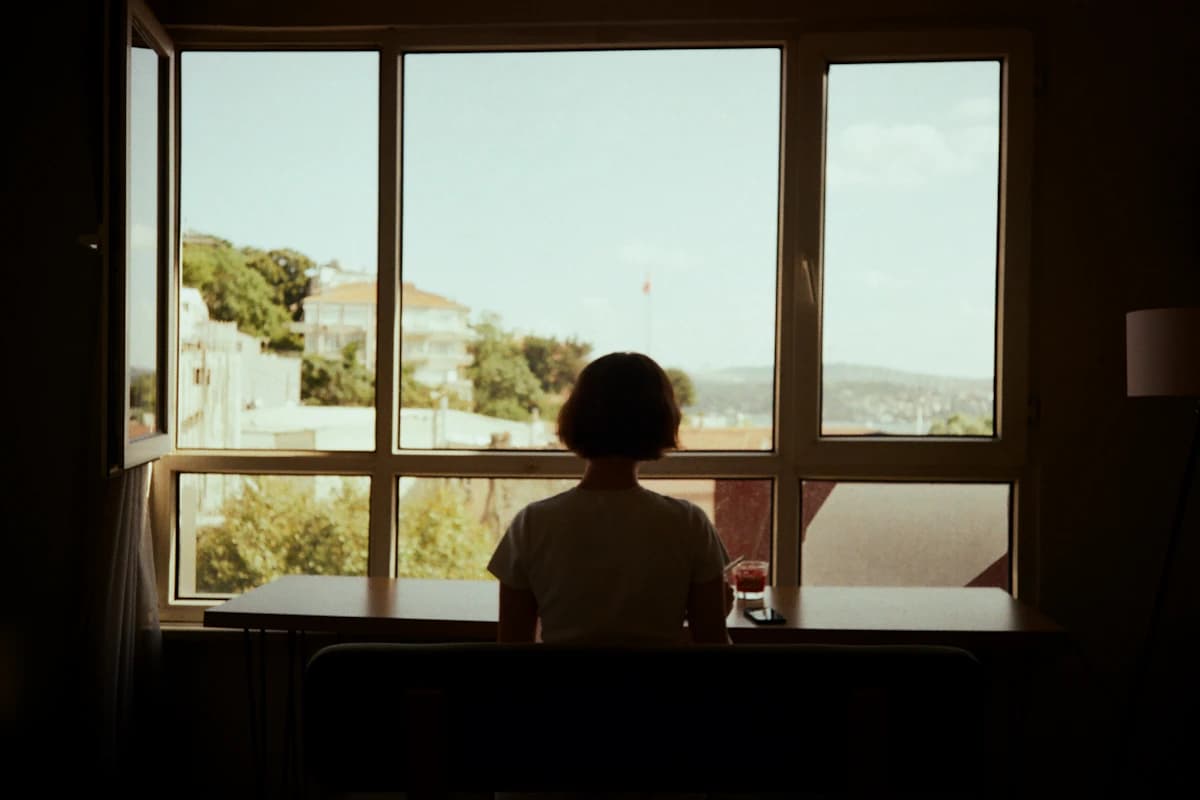 A person sitting quietly by a large window, shown as representative lifestyle imagery